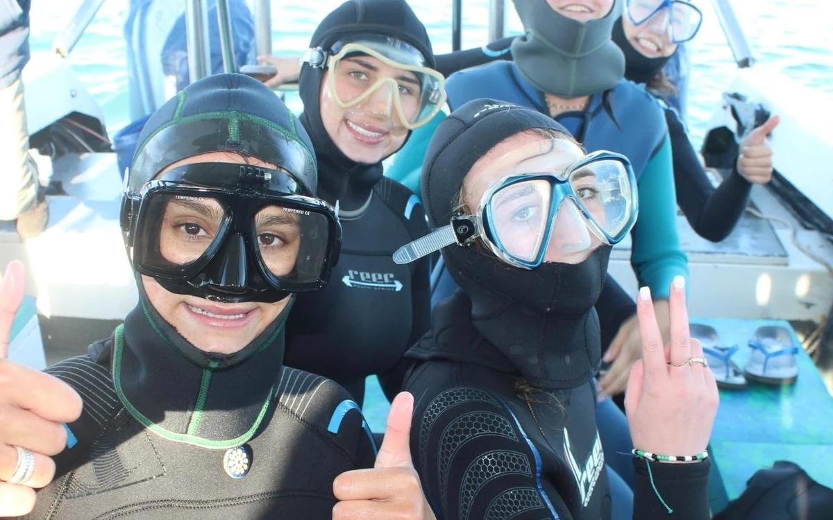 Tres personas con trajes de neopreno y máscaras de buceo en el barco, pulgares arriba antes de entrar